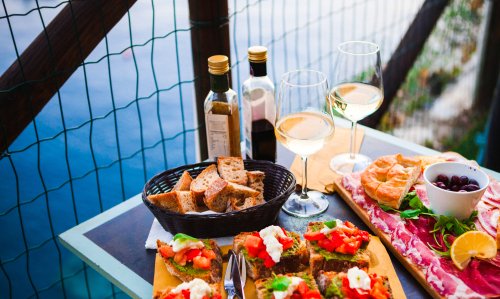 Romantic dinner for two at sunset. White wine and Tasty italian snack: fresh bruschettes and meat on the board in outdoor cafe with amazing view in Manarola, Italy